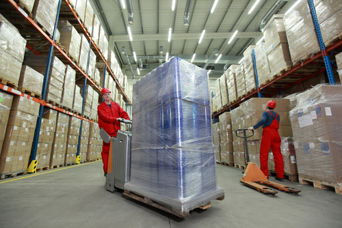 two workers in uniforms and safety helmets working in storehouse