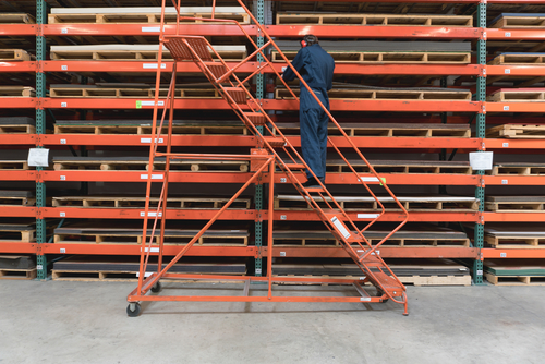 man on ladder with stacking racks and stored pallets