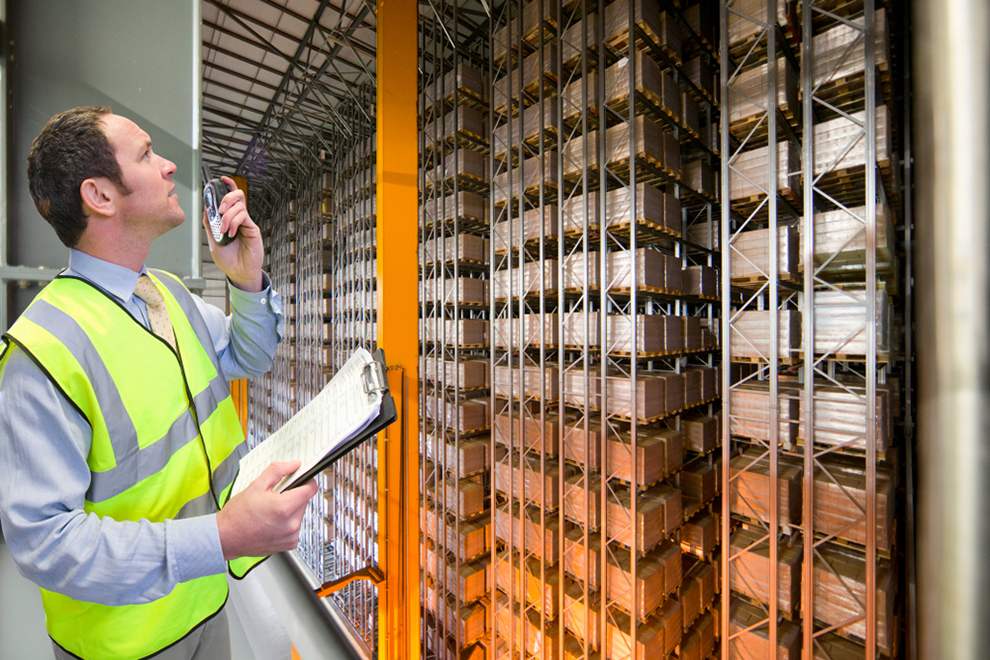 a worker with a walkie talkie and a clipboard surveying a warehouse
