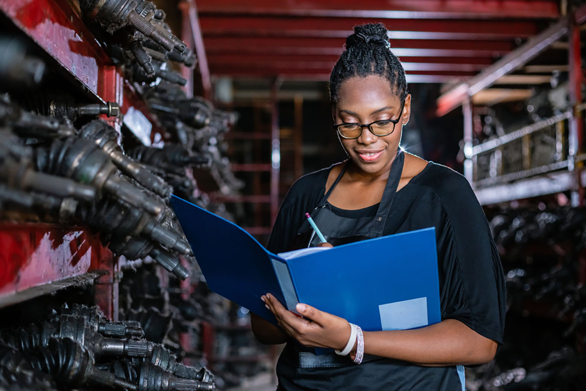 African american worker woman wear spectacles crossed arms holding clipboard standing in factory auto parts. female employee business warehouse motor vehicle.